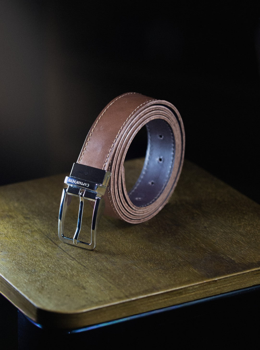 Brown leather belt with silver buckle on a wooden surface