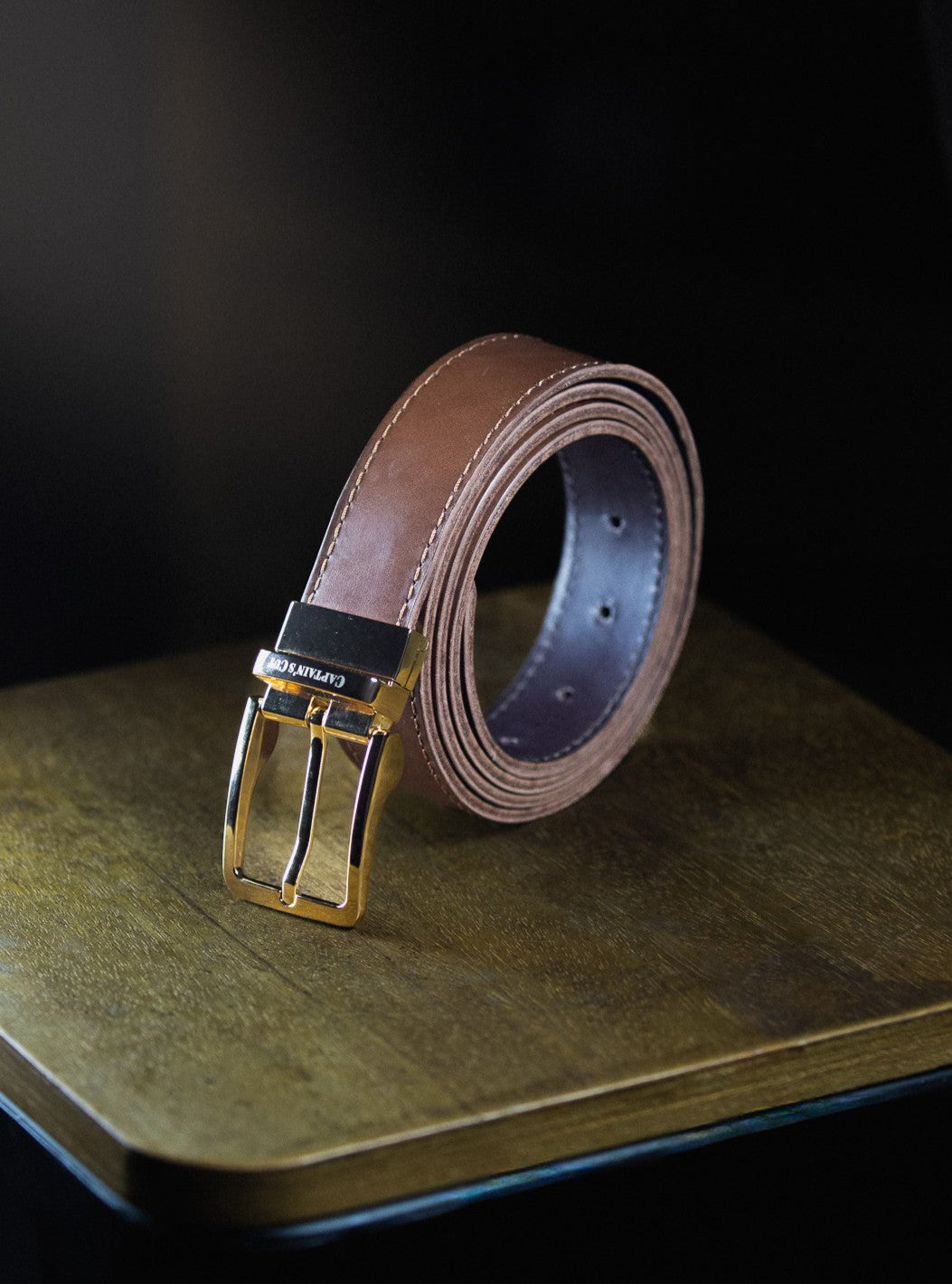 Brown leather belt with silver buckle on a wooden surface