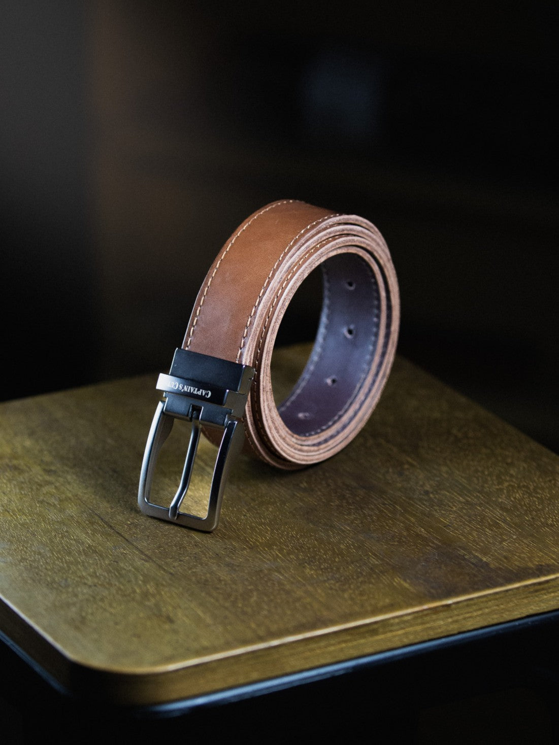 Brown leather belt with silver buckle on a wooden surface