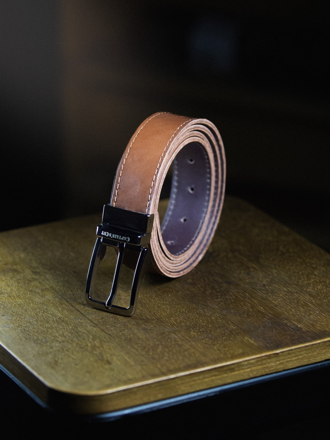 Brown leather belt with black buckle on a wooden surface