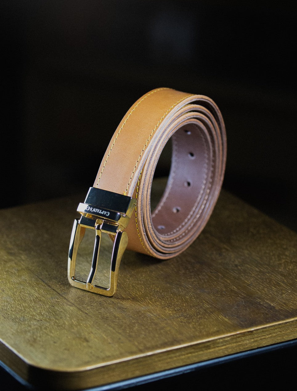 Cognac leather belt with golden buckle on a wooden surface