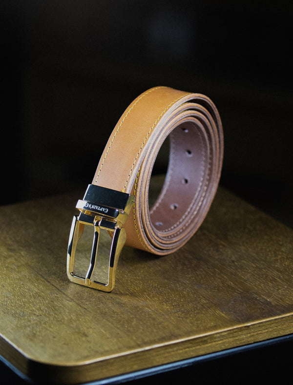 Cognac leather belt with golden buckle on a wooden surface