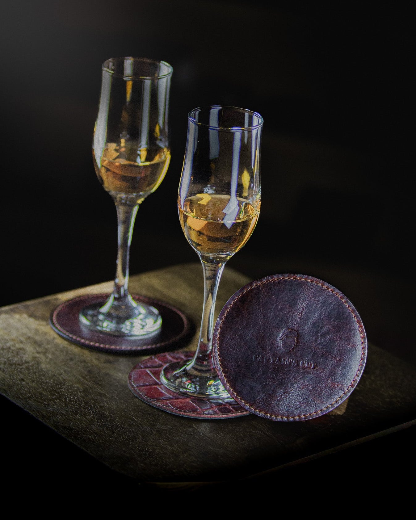 two glasses of wine on coasters standing on a wooden surface on a black backgroung