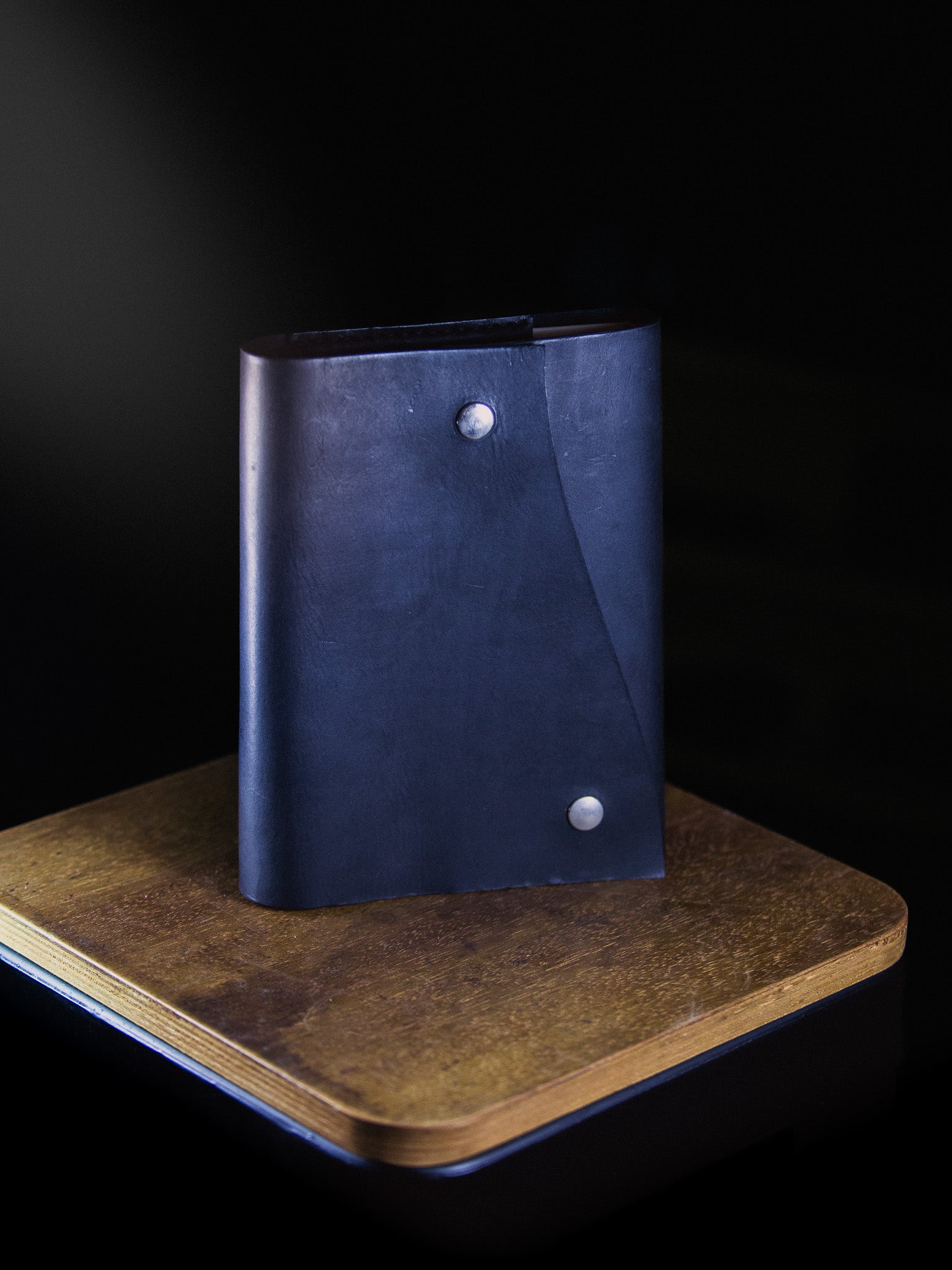 Blue leather notebook with silver buttons on a wooden stand against a black background