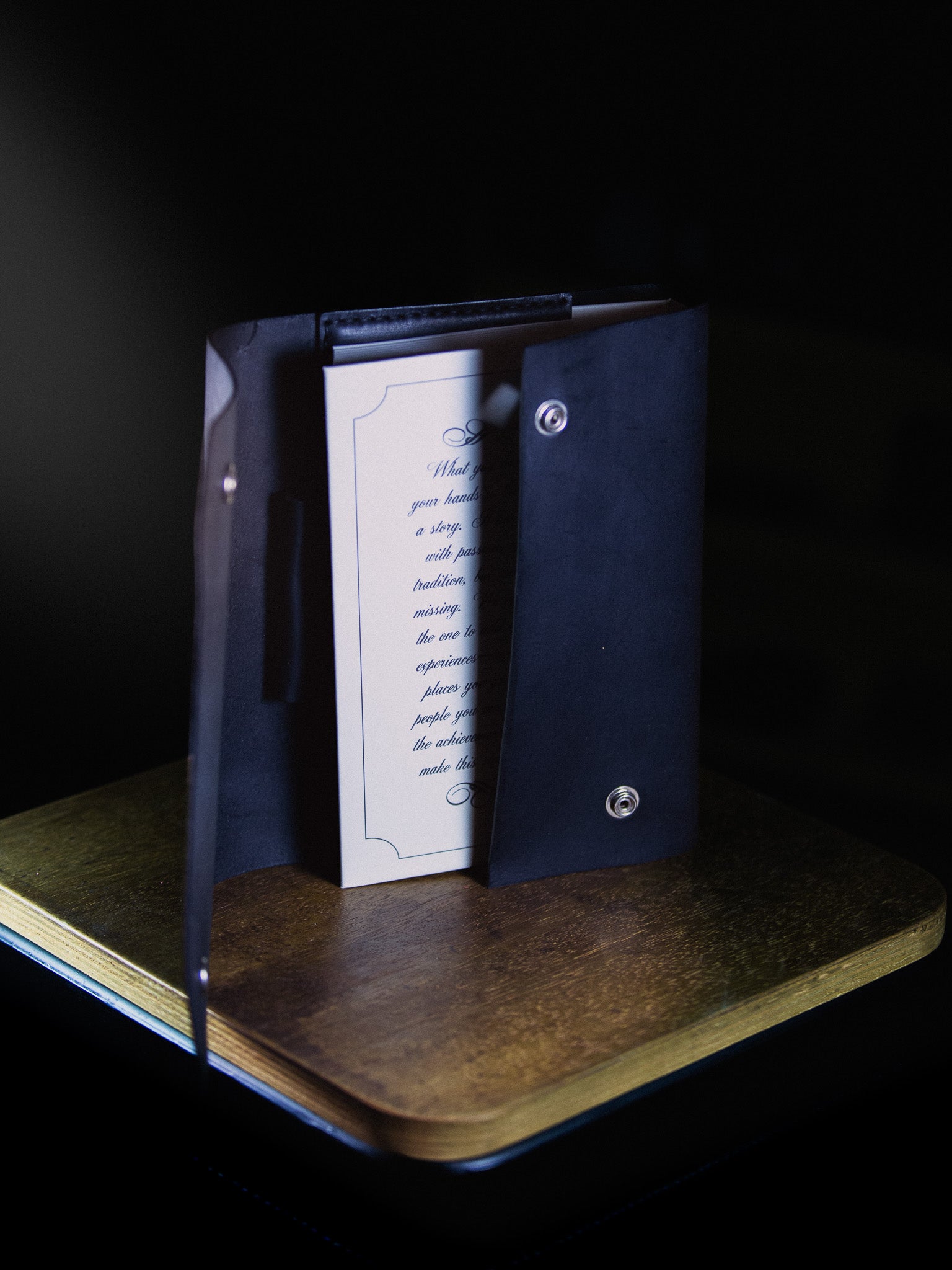 Black leather-bound book with a clear plastic cover on a wooden surface