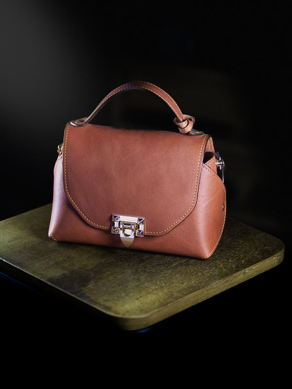 Brown leather handbag on a dark surface with a black background