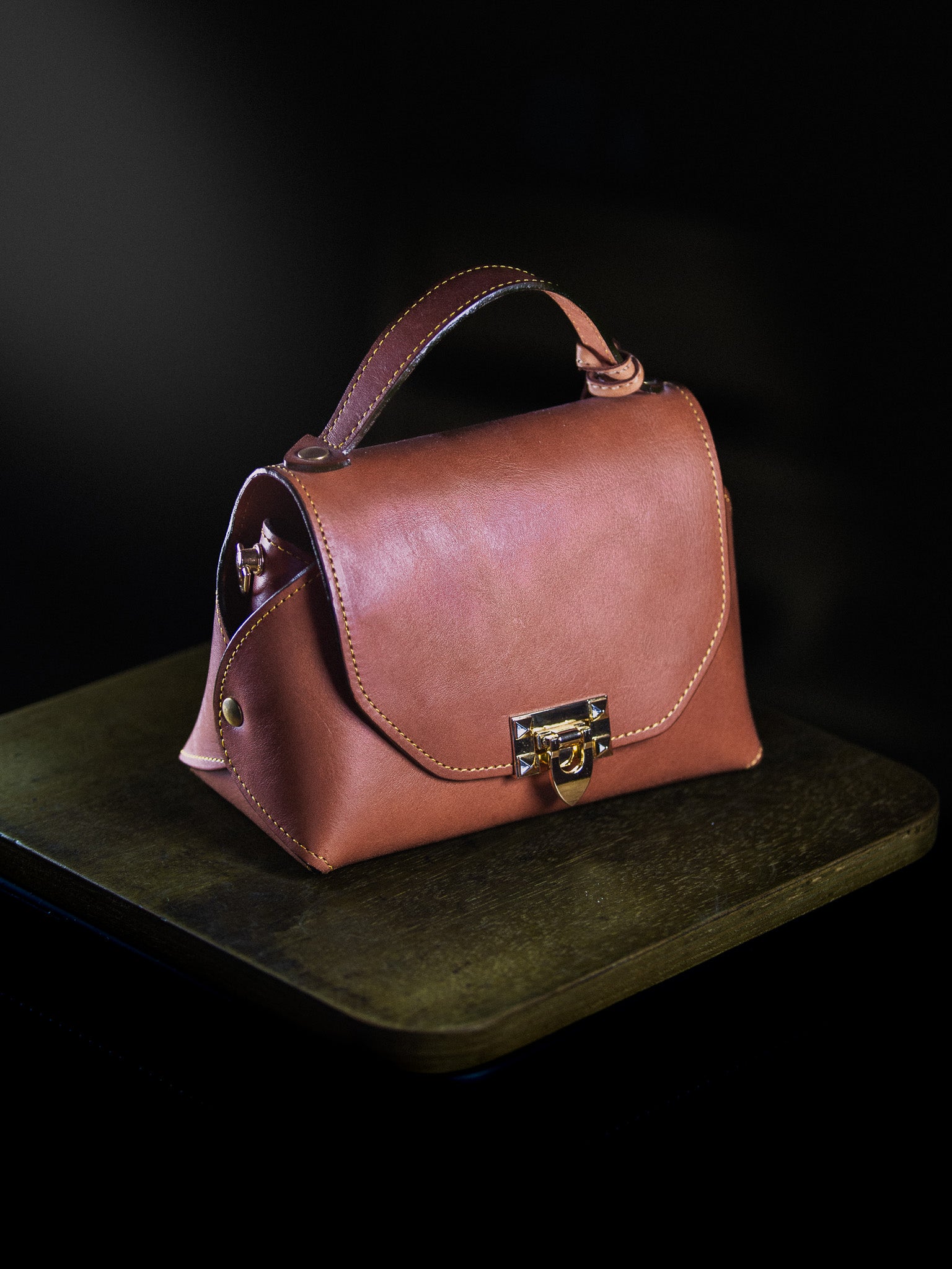 Brown leather handbag with a gold lock on a dark surface