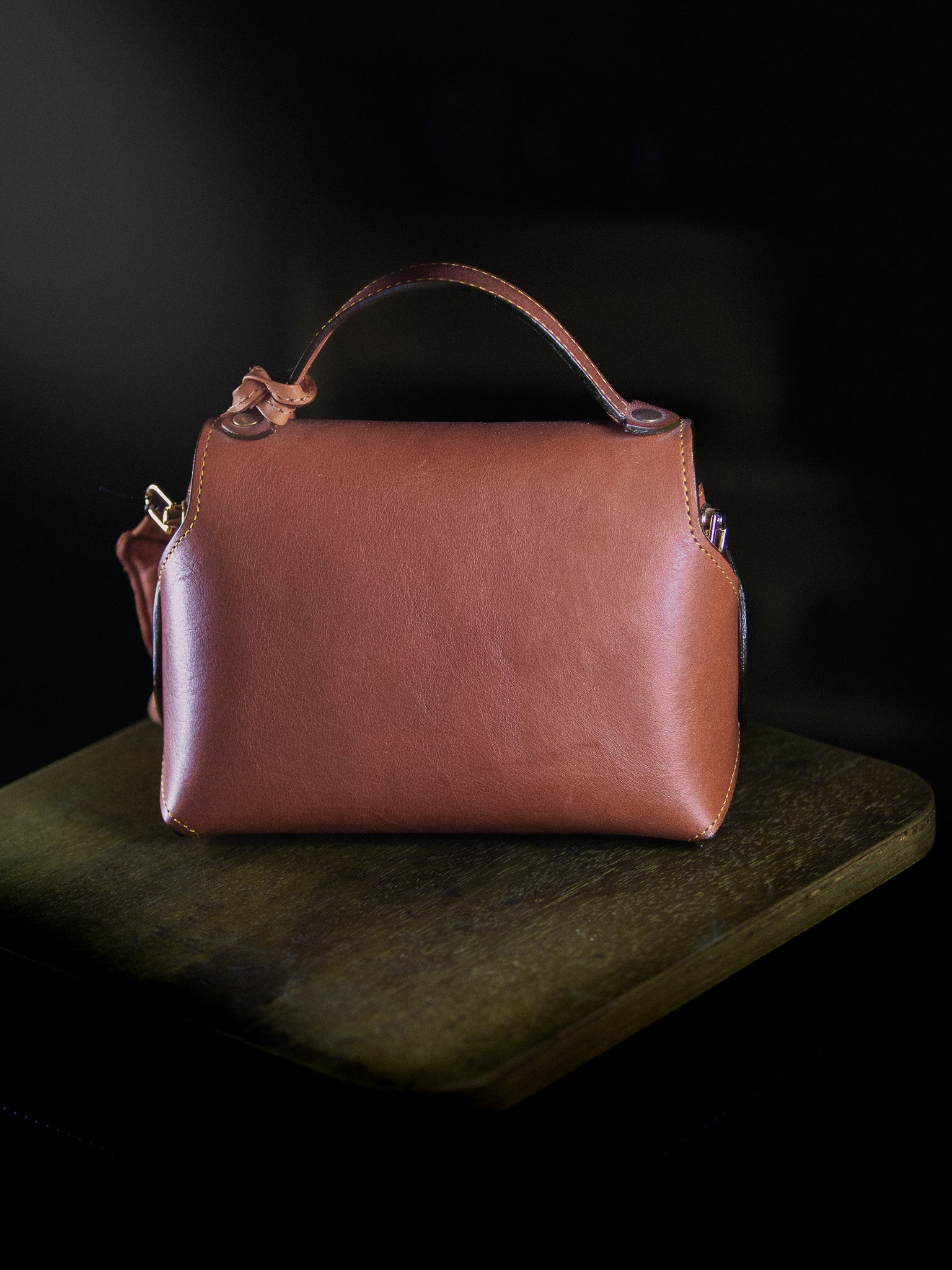 Brown leather handbag with a gold lock on a dark surface