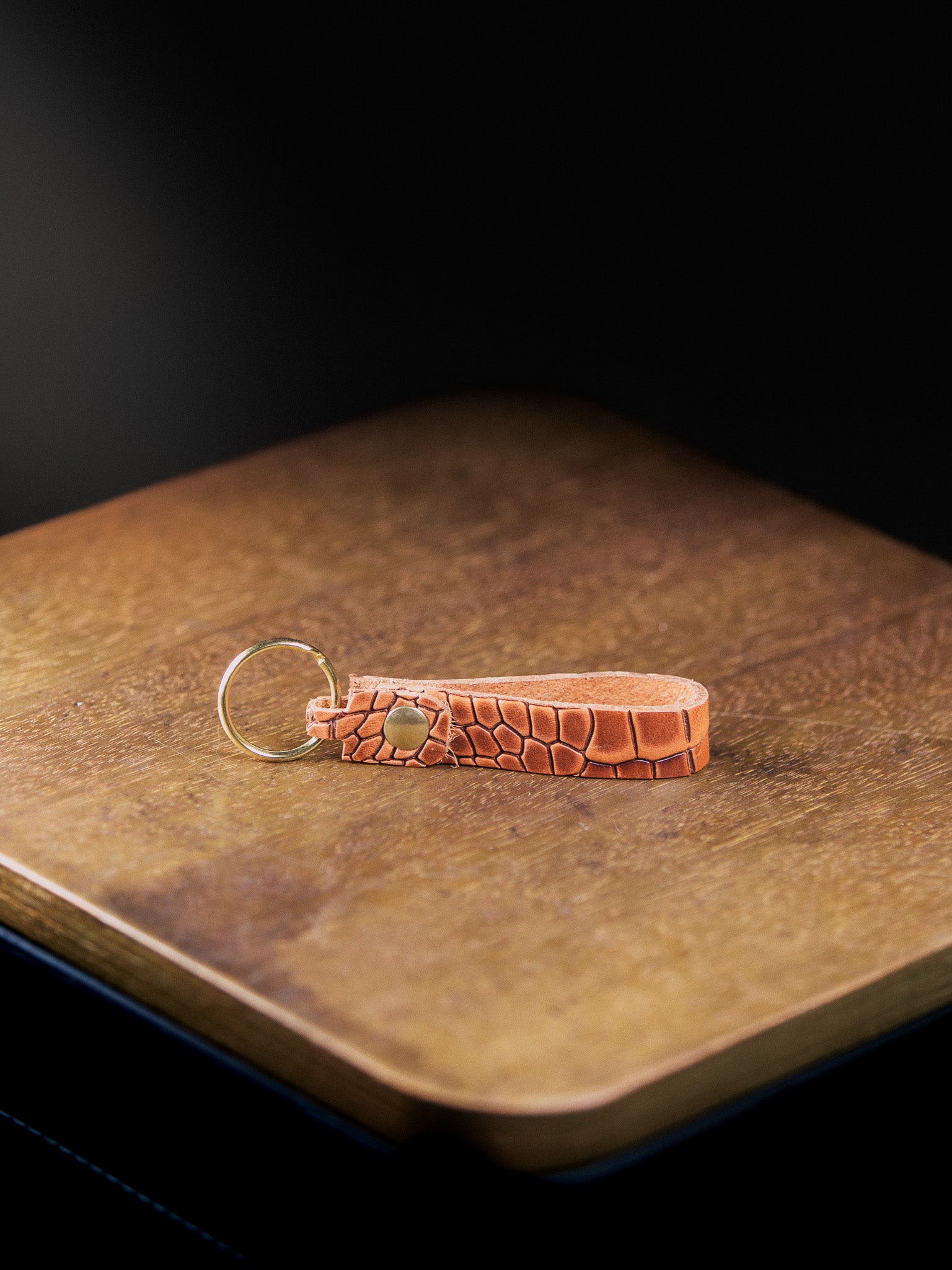 Brown leather keychain on a wooden surface with a dark background