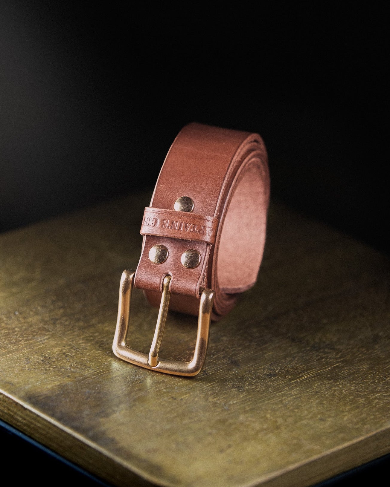 Brown leather belt with brass buckle on a dark surface