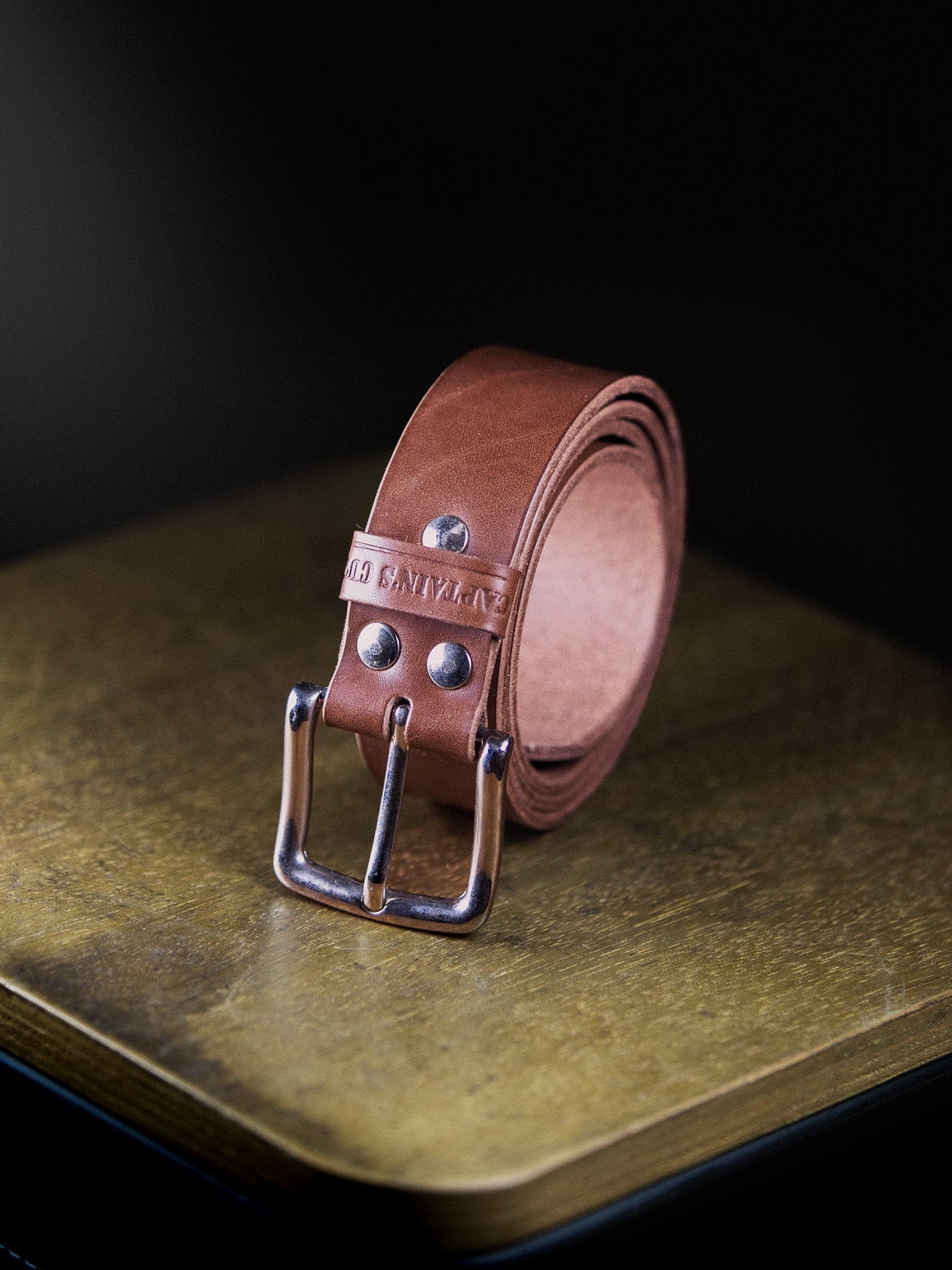 Brown leather belt with silver buckle on a dark surface