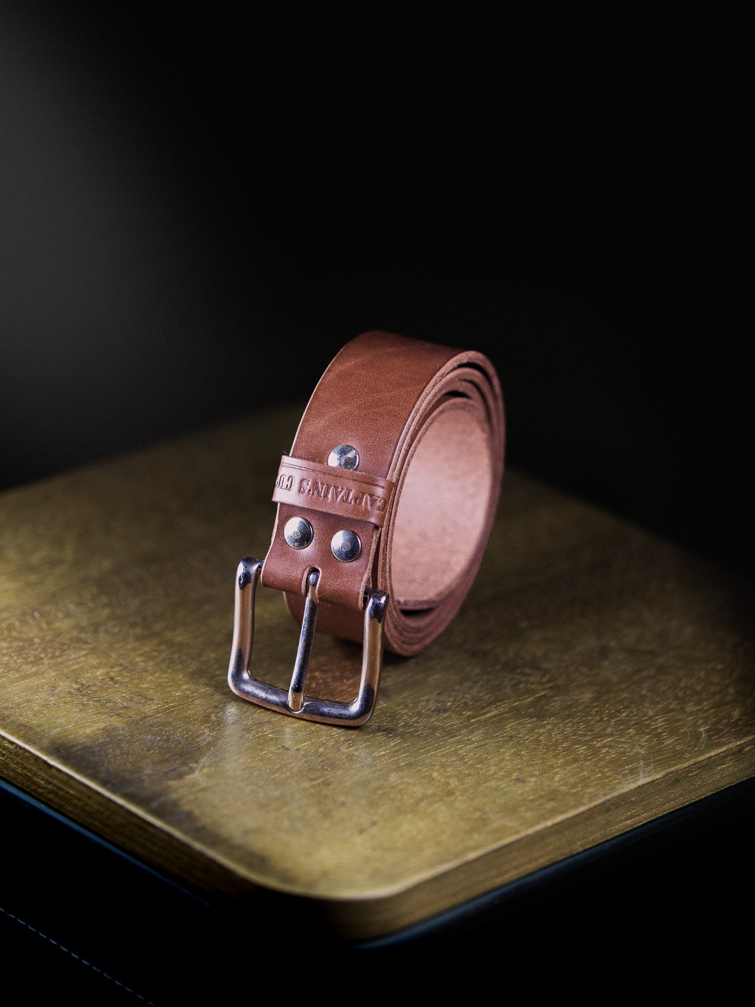 Brown leather belt with silver buckle on a dark surface