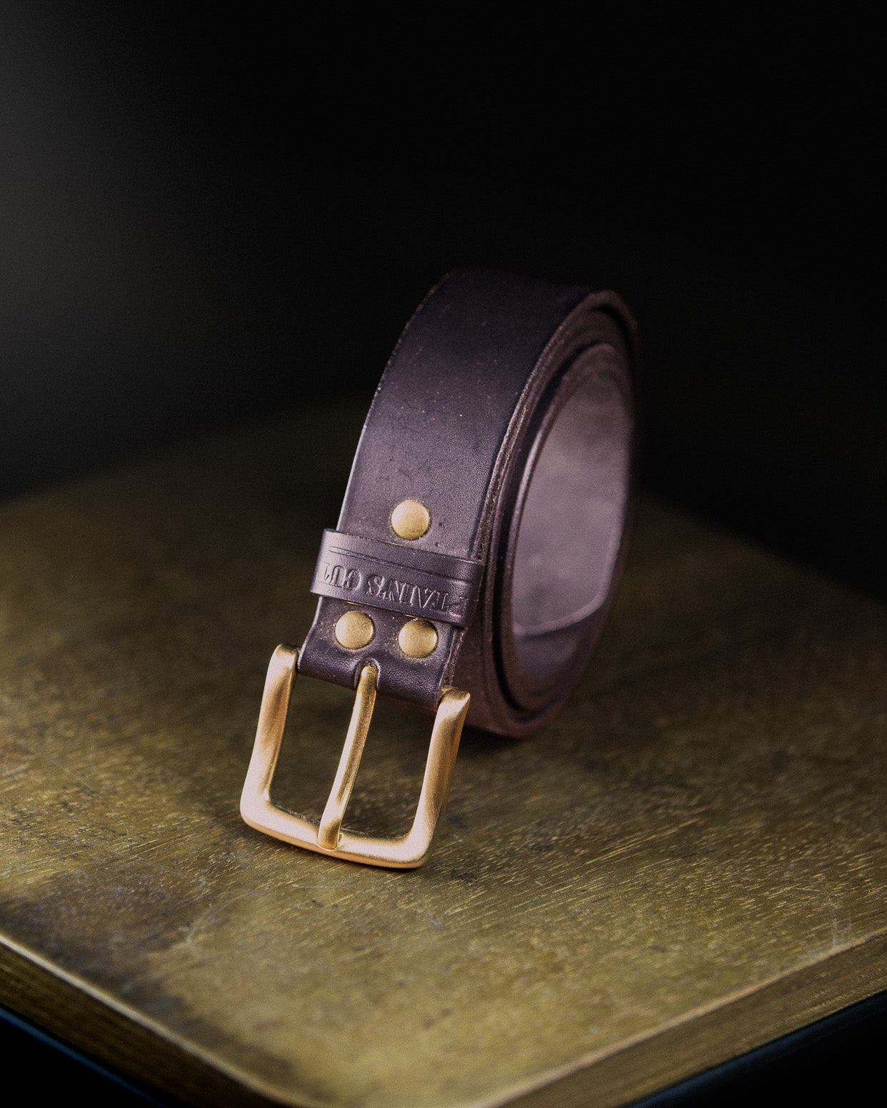 Brown leather belt with brass buckle on a dark surface