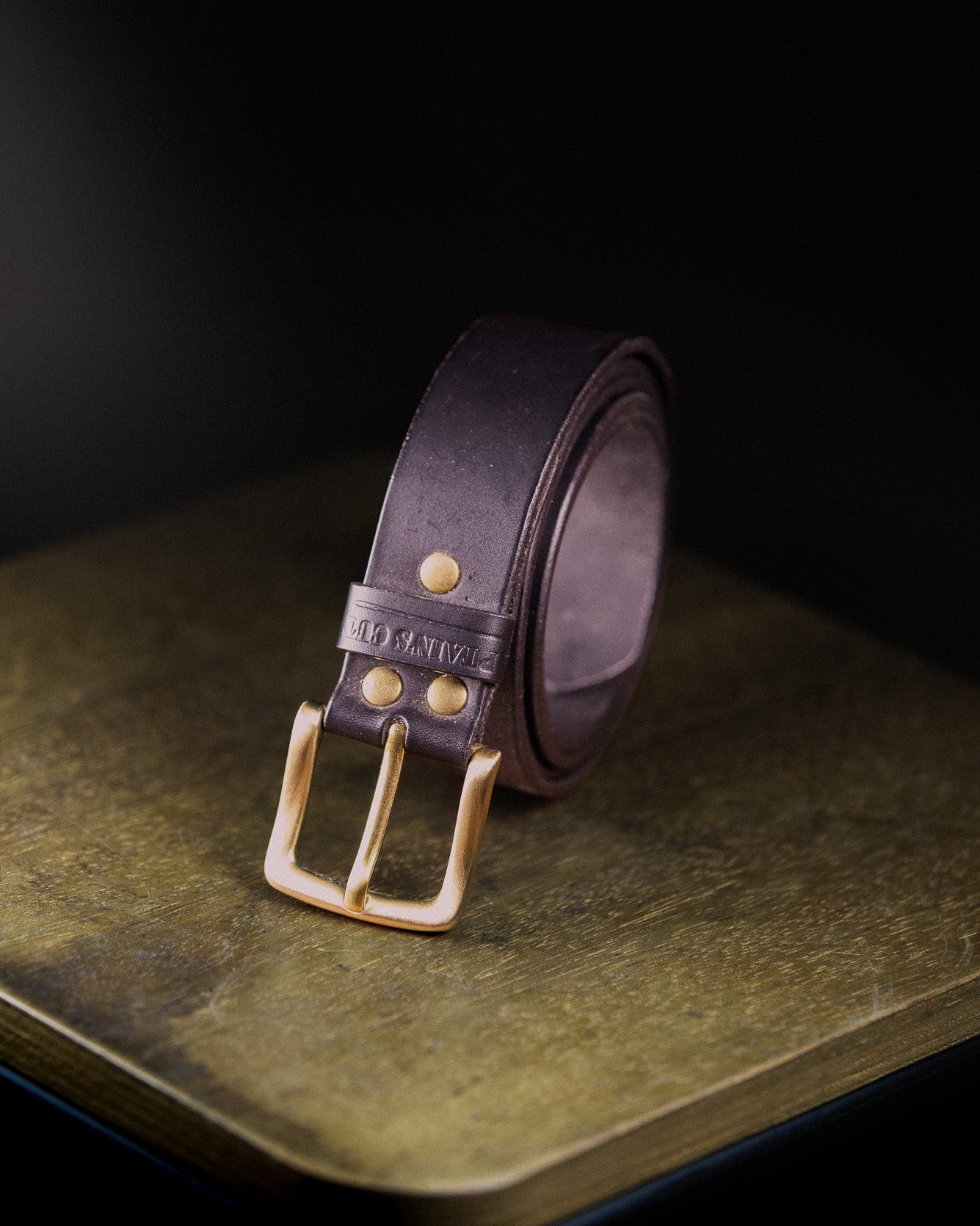 Brown leather belt with brass buckle on a dark surface