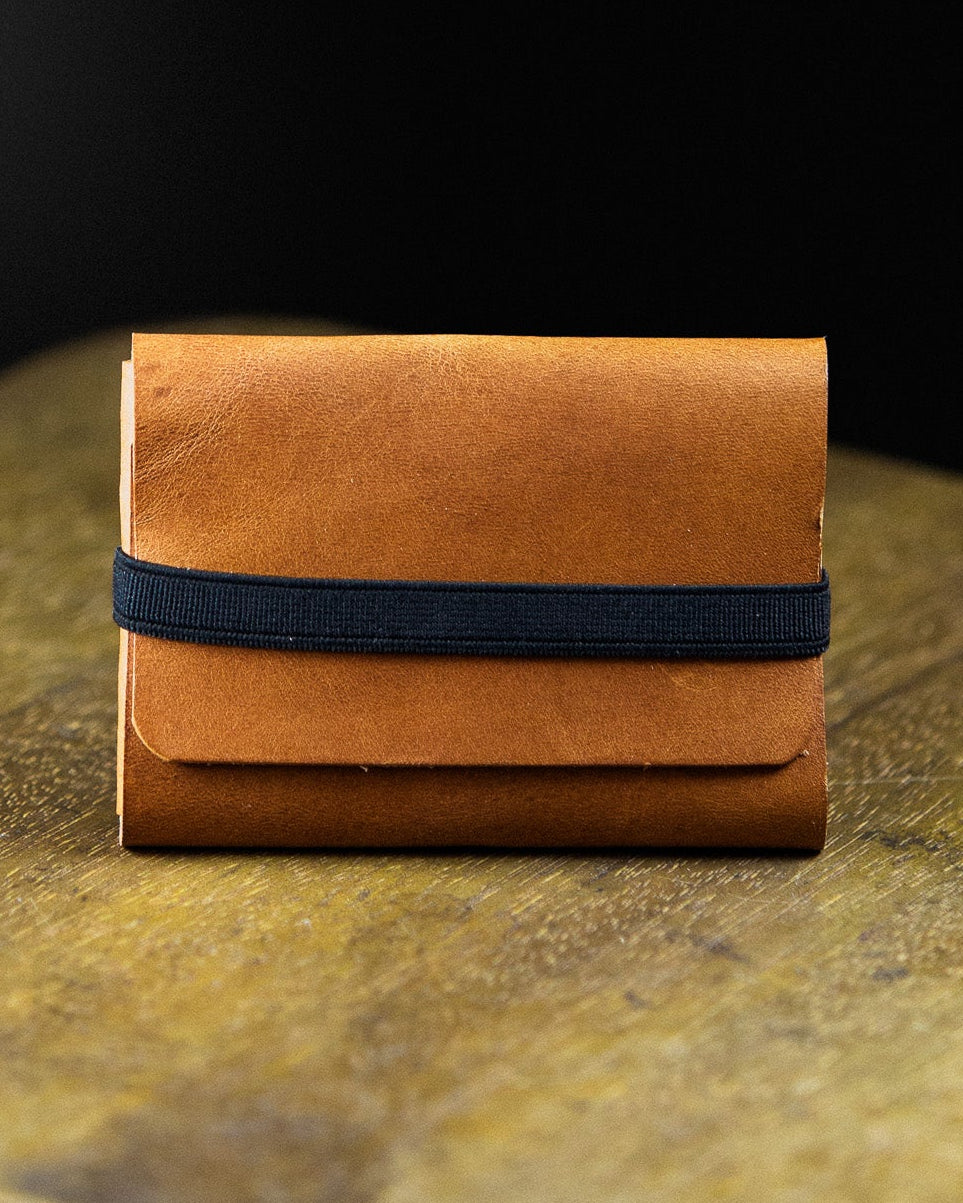 Brown leather wallet with a black strap on a dark surface