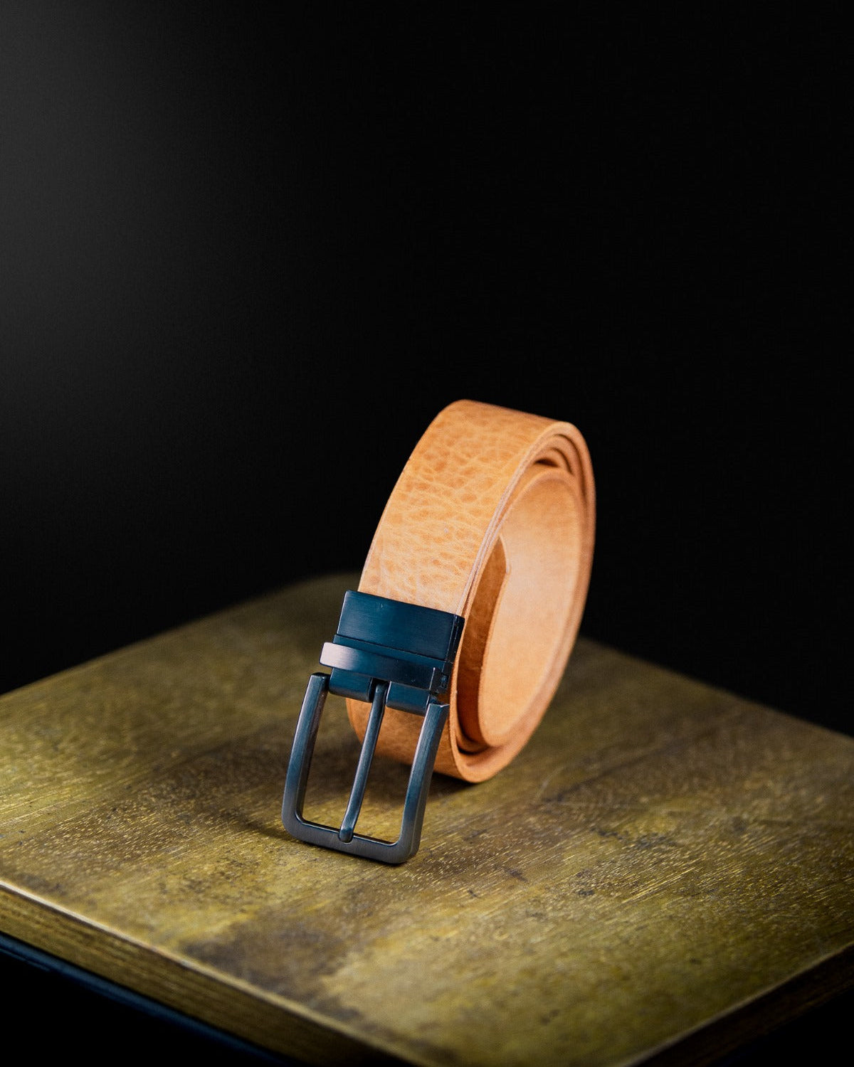 Cognac Leather Belt with matte chrome buckle on a wooden surface on a dark background