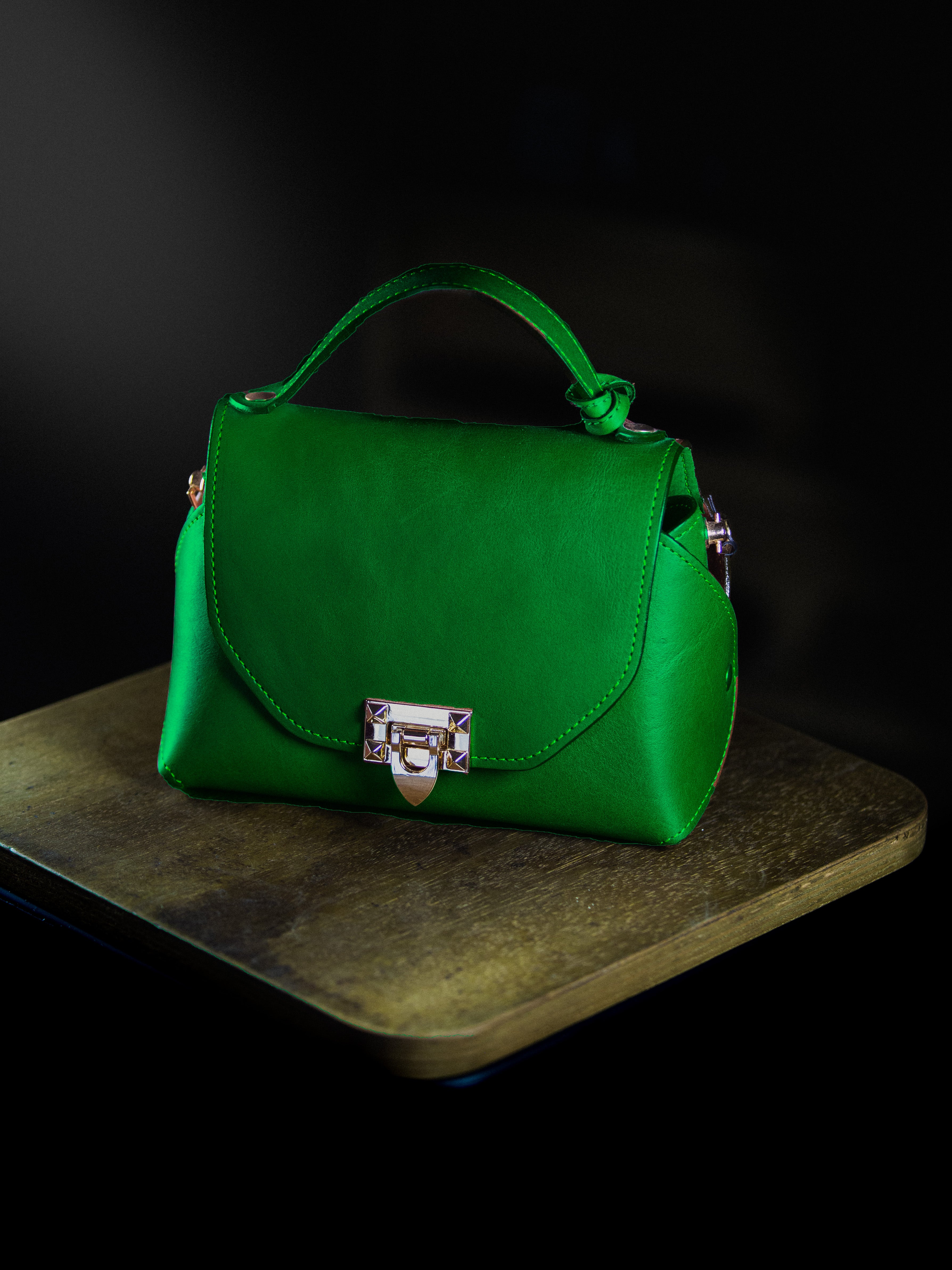 Green leather handbag with a silver lock on a dark surface